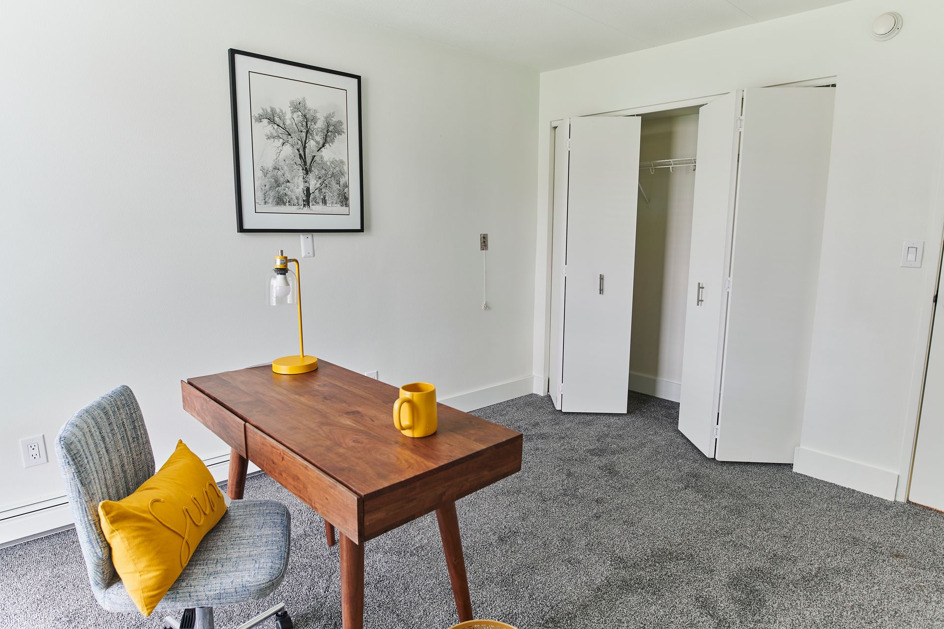 A room with a desk , chair , lamp and a picture on the wall.