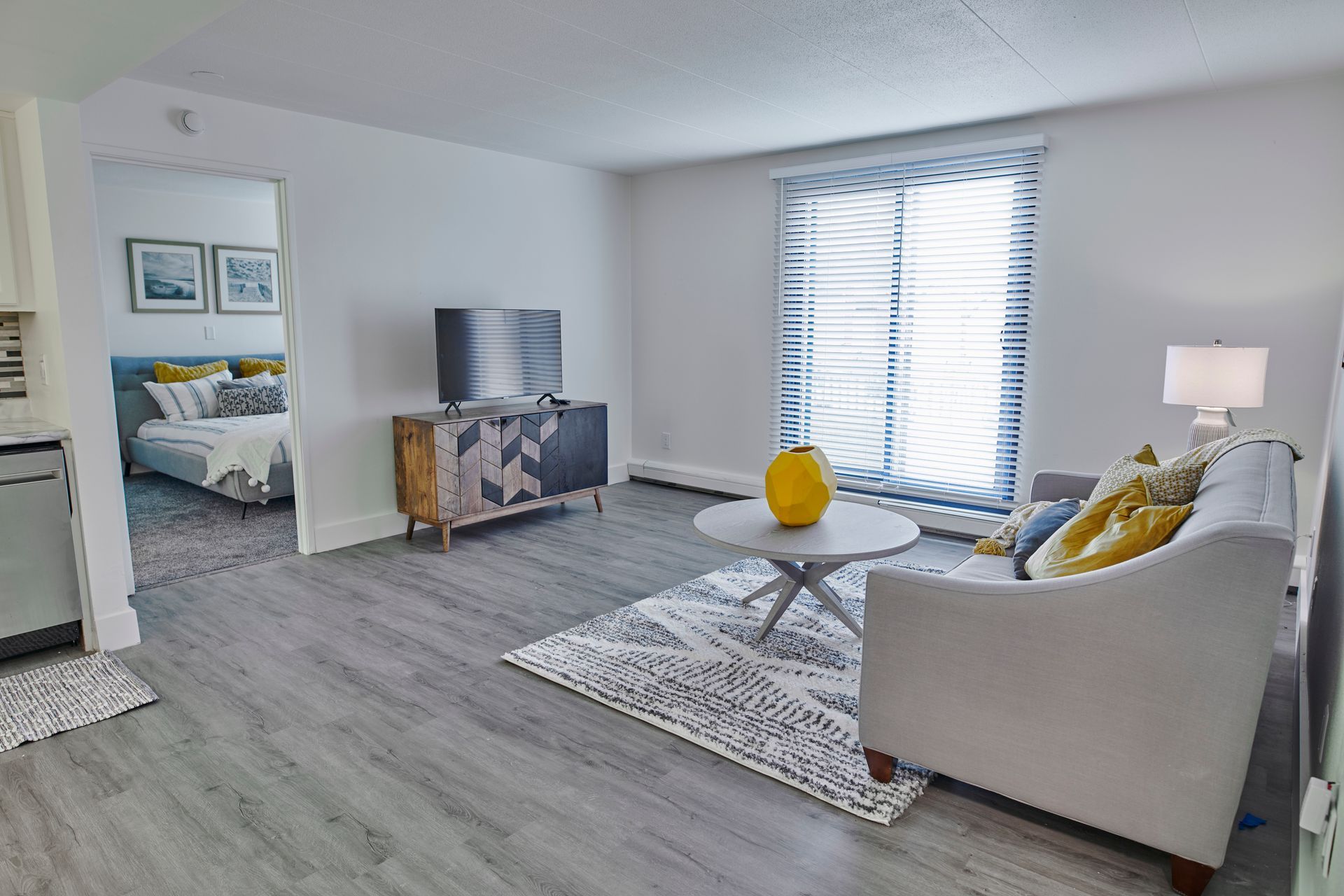 A living room with a couch , coffee table , television and sliding glass doors leading to a bedroom.