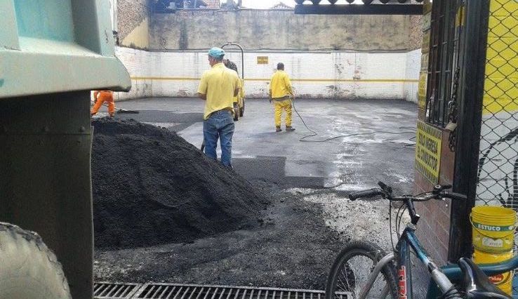 Trabajador de la construcción con chaleco de seguridad naranja y casco alisando hormigón con una paleta.