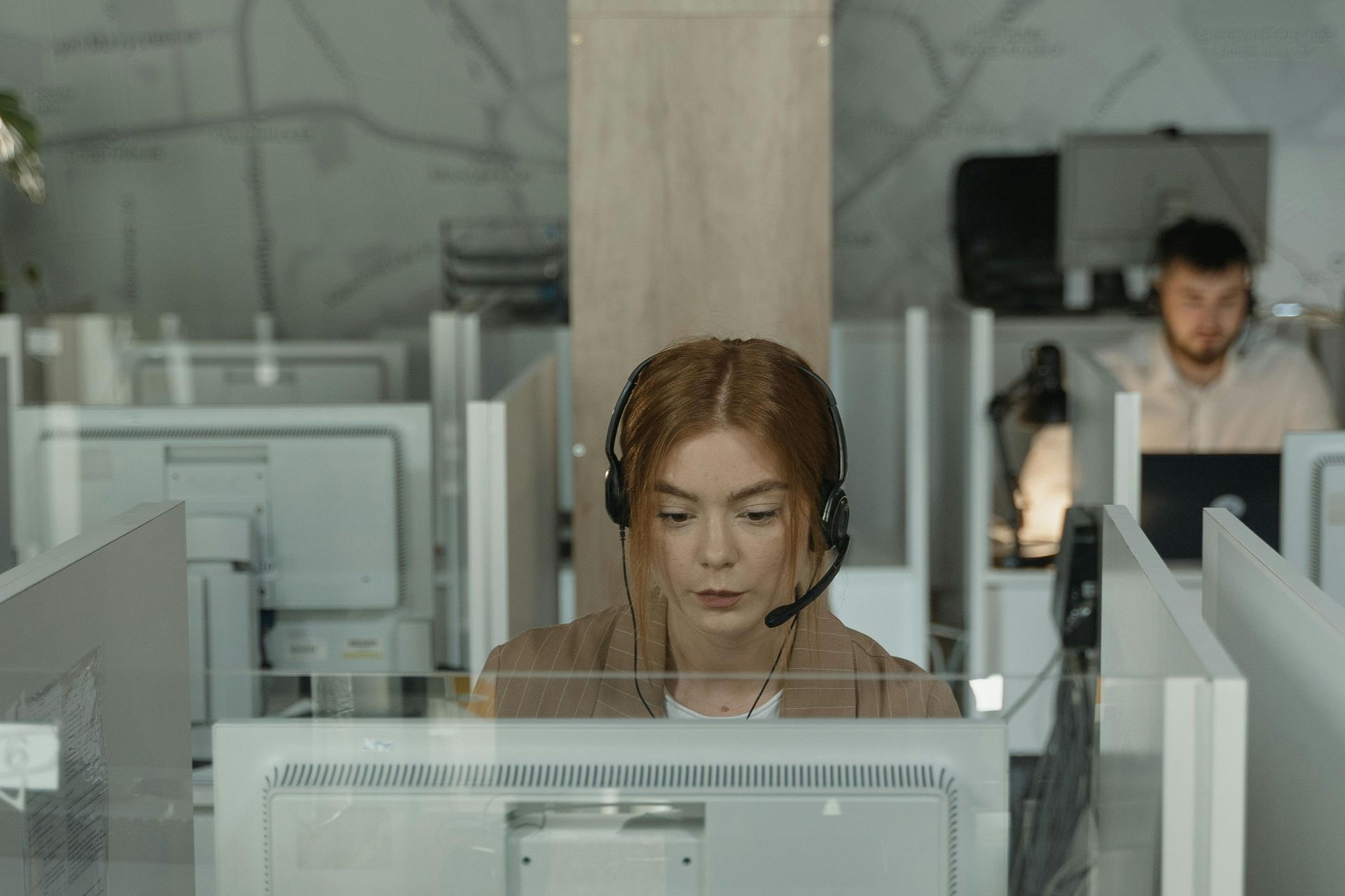 A woman wearing a headset is sitting in front of a computer in a call center.