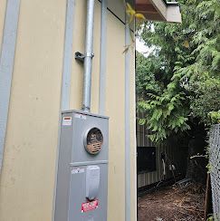An outdoor electrical meter box mounted on a yellow exterior wall with a metal conduit running up toward the roofline.