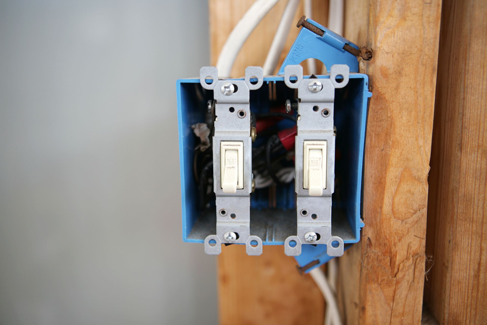 A double-gang electrical box mounted to a wooden stud, containing two light switches and visible interior wiring.