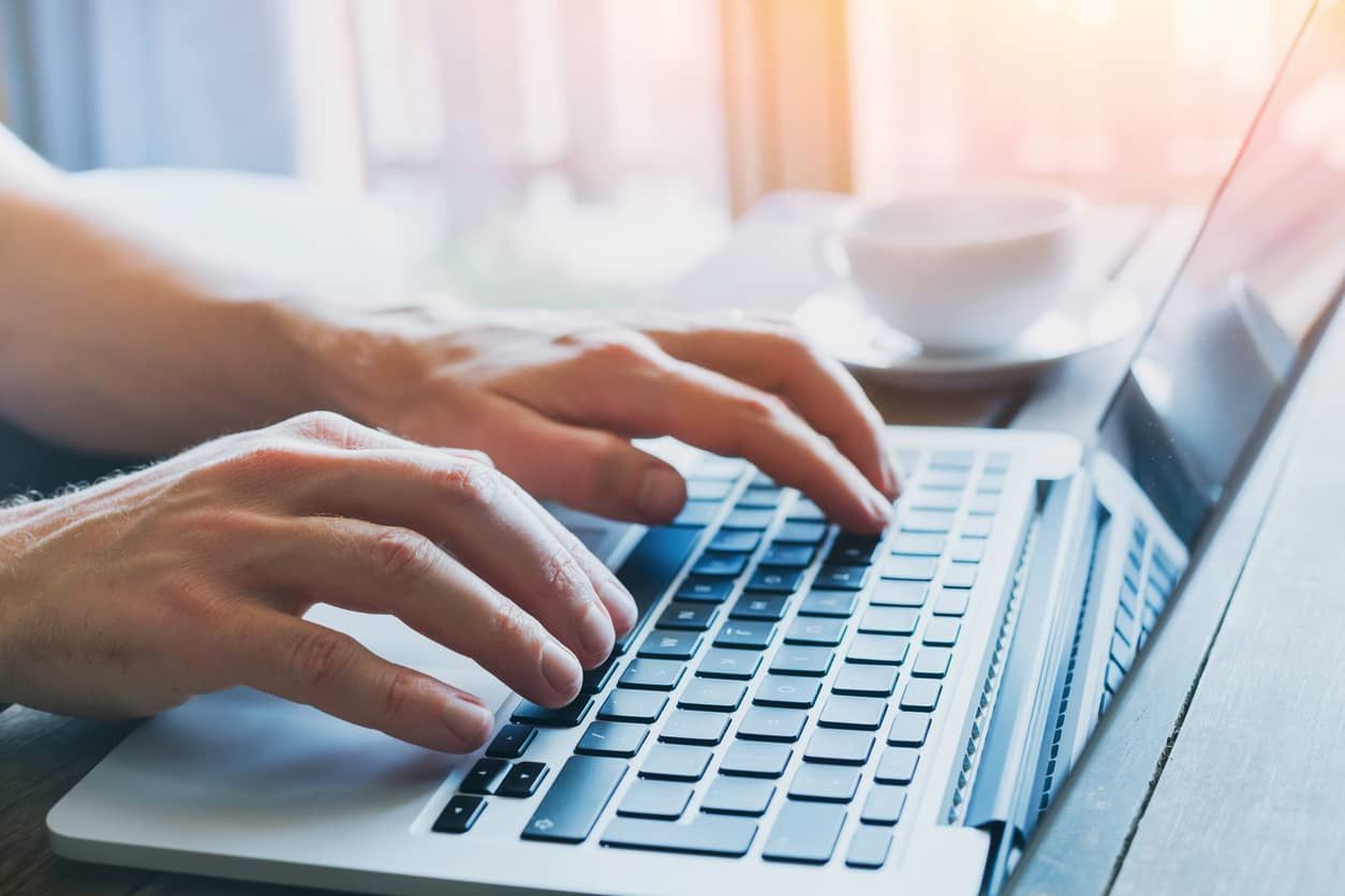 A person is typing on a laptop computer with a cup of coffee in the background.