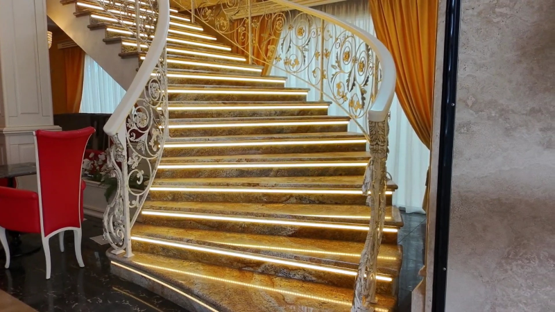 Una scala a chiocciola con gradini dorati e una ringhiera in ferro battuto in una stanza.