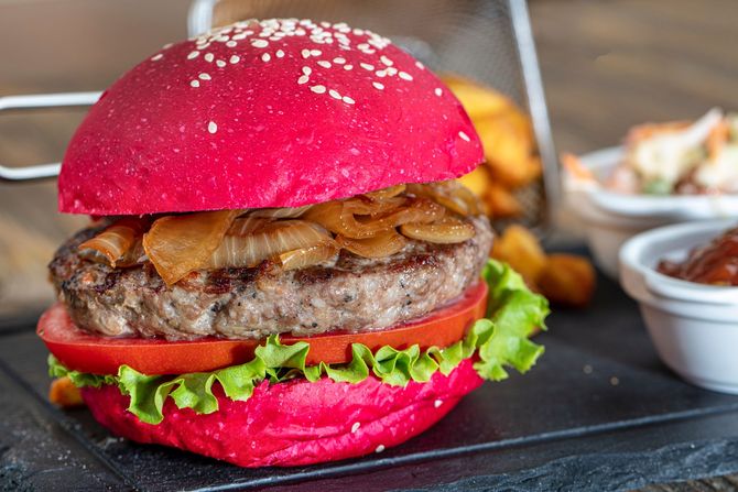 Un primo piano di un hamburger con un panino rosso su un tavolo.