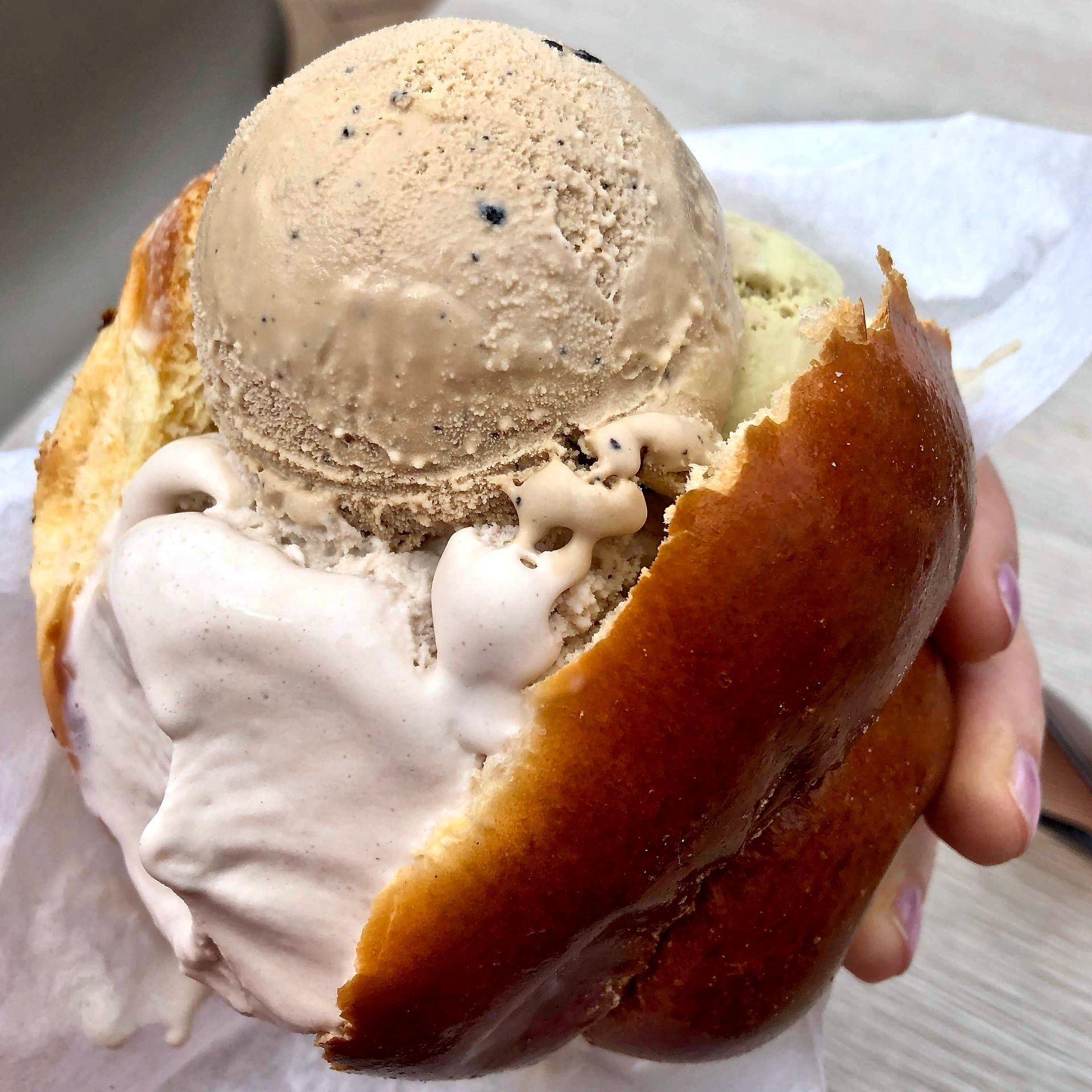 Una persona tiene in mano un panino con del gelato sopra