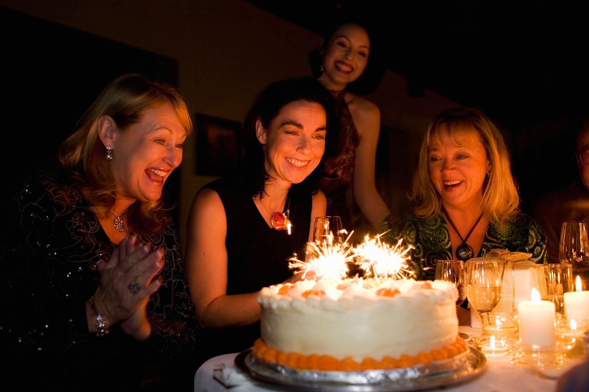 Un gruppo di donne è seduto attorno a una torta di compleanno con delle stelle filanti.