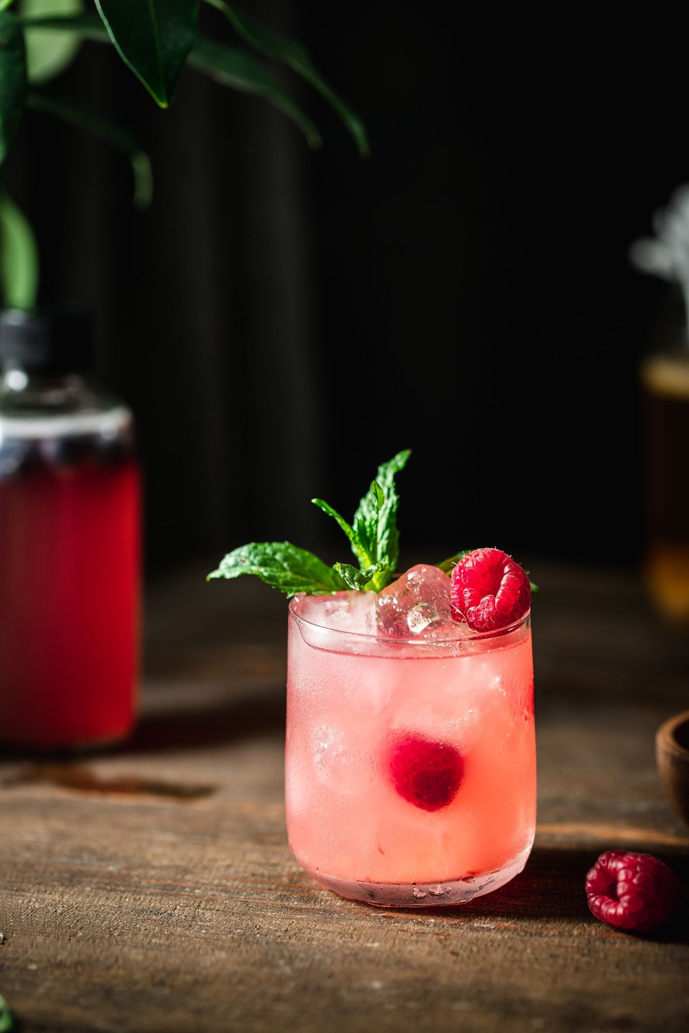 Un bicchiere di liquido rosa con lamponi e menta su un tavolo di legno.