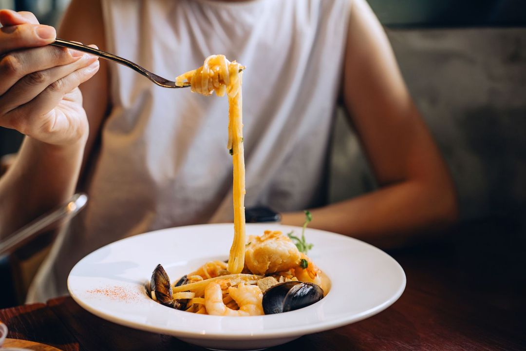 Una persona sta mangiando la pasta con una forchetta da un piatto.