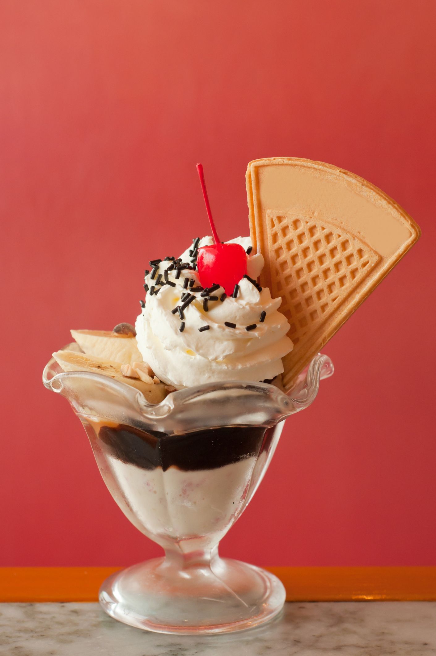 Su un tavolo c'è un gelato con panna montata e una ciliegia sopra.