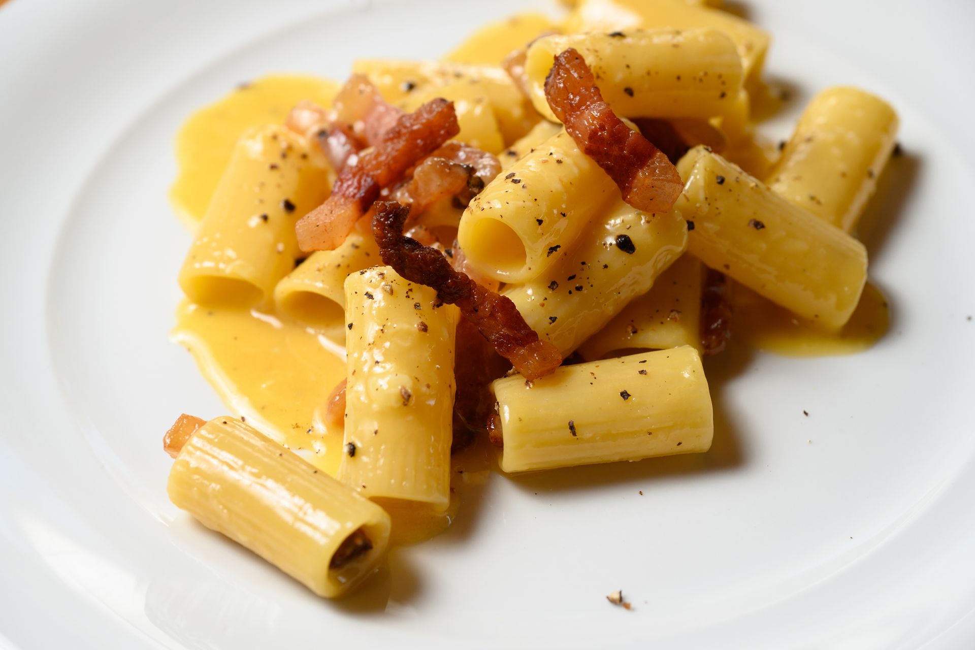 Un piatto bianco condito con maccheroni e formaggio e pancetta