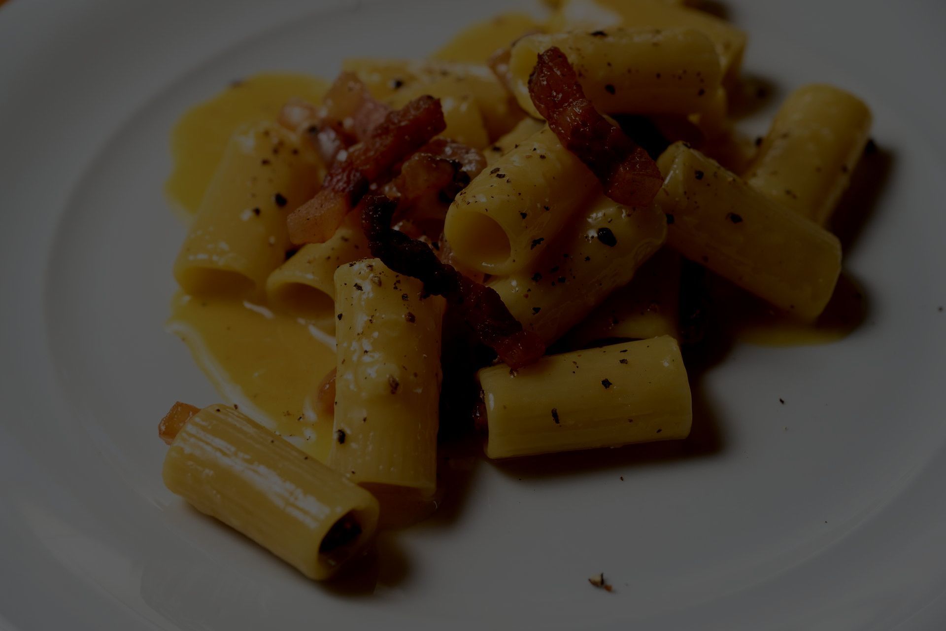 Un primo piano di un piatto di pasta con sugo e pancetta su un tavolo.