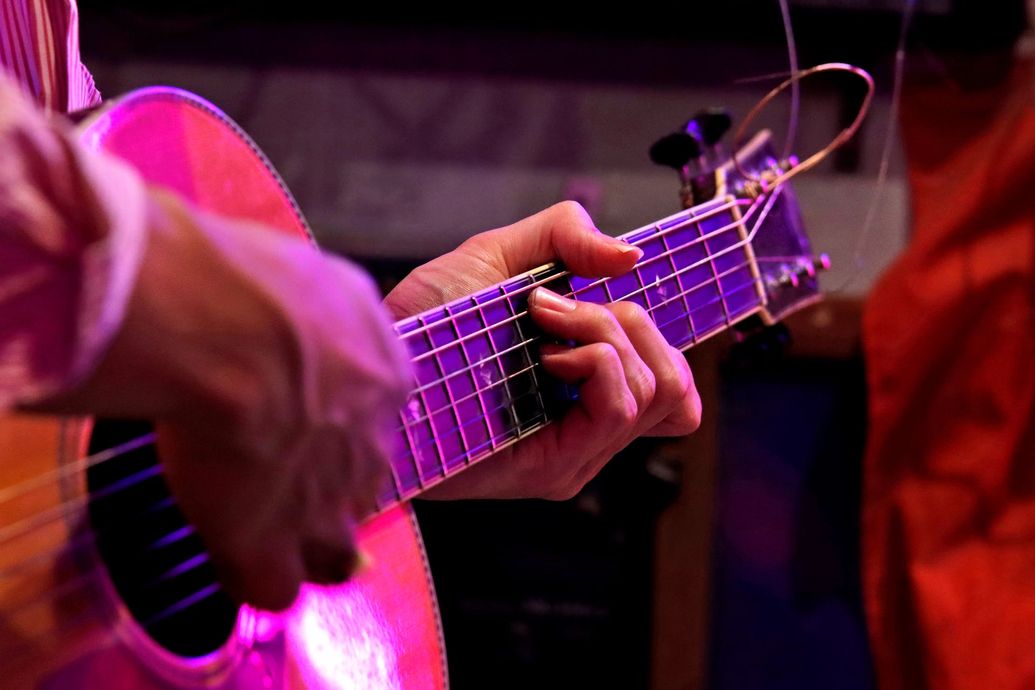 Una persona sta suonando una chitarra acustica in una stanza buia.