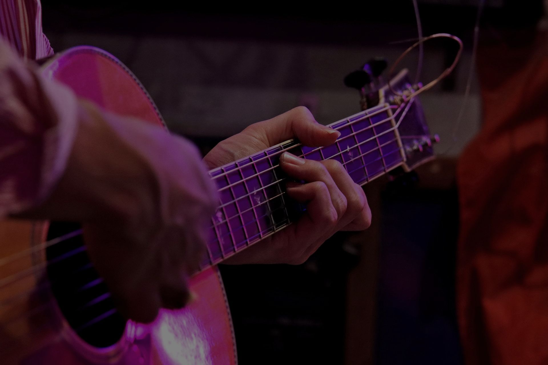 Una persona sta suonando una chitarra acustica in una stanza buia.