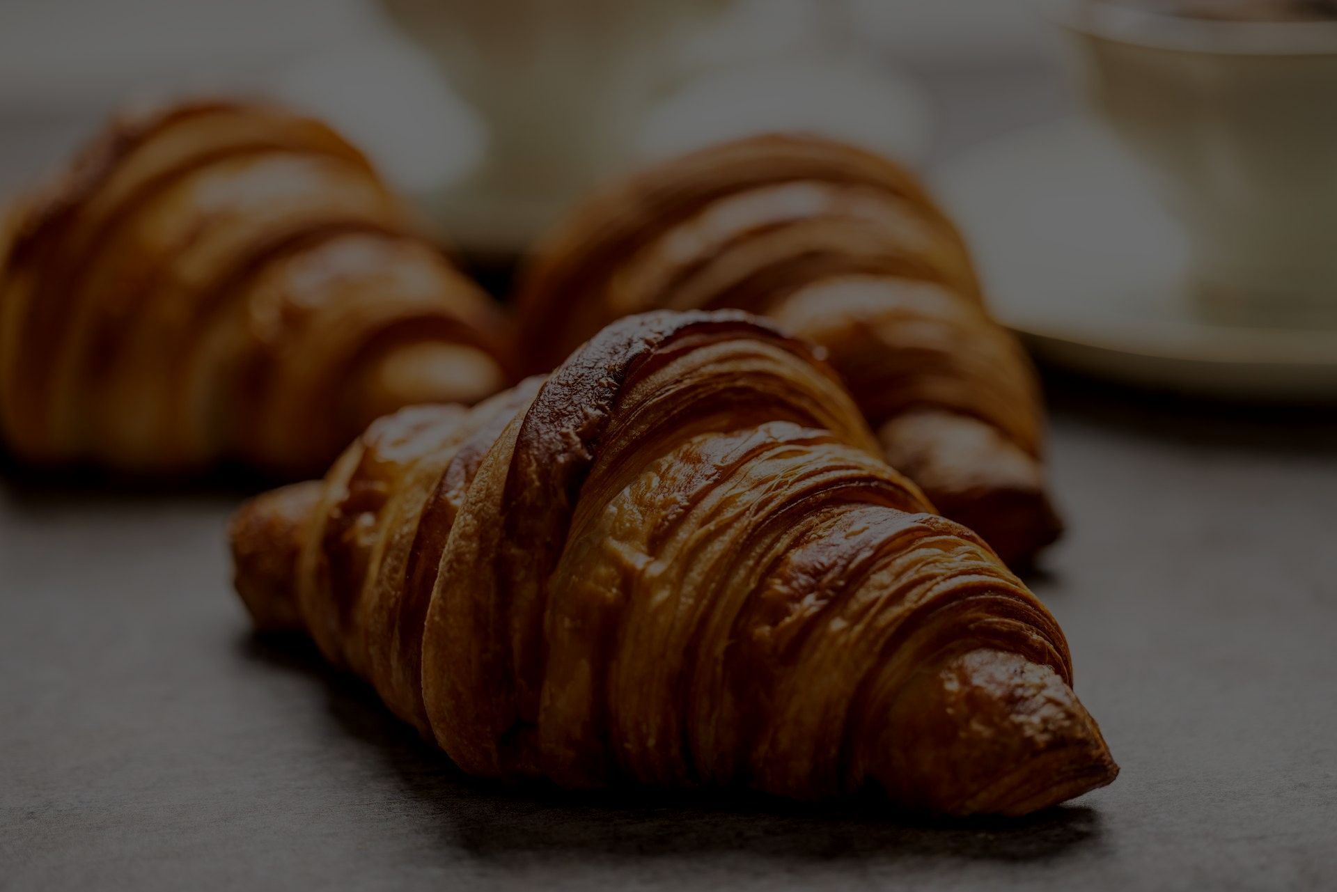 Tre croissant sono appoggiati su un tavolo accanto a una tazza di caffè.