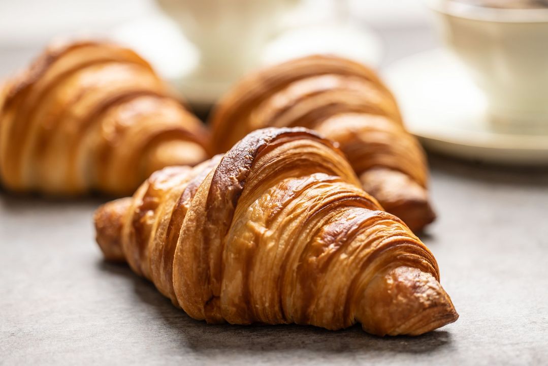 Tre croissant sono appoggiati su un tavolo accanto a una tazza di caffè.