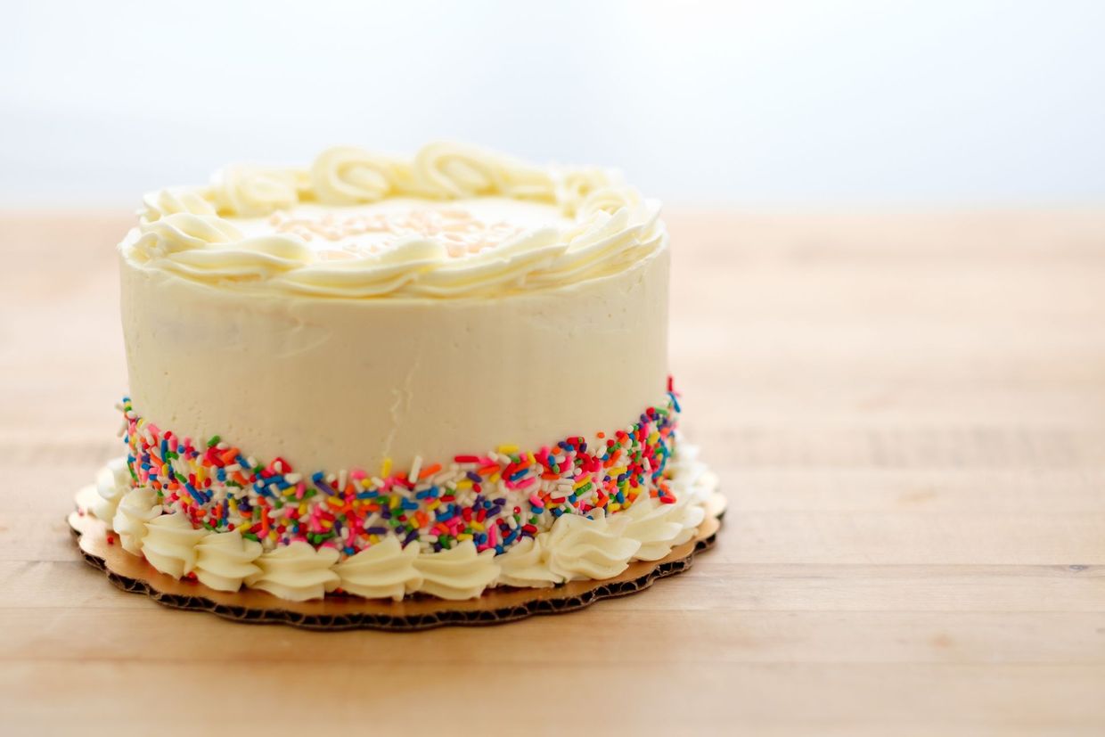 Una torta di compleanno con glassa bianca e granelli di zucchero su un tavolo di legno.