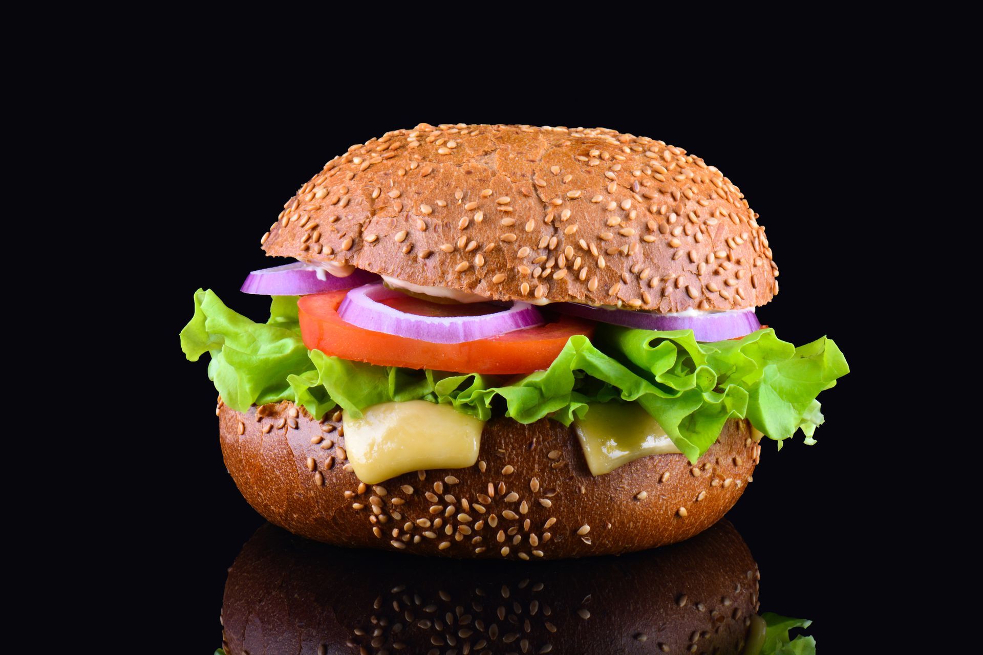 Un hamburger con lattuga, pomodoro, cipolle e formaggio su uno sfondo nero.