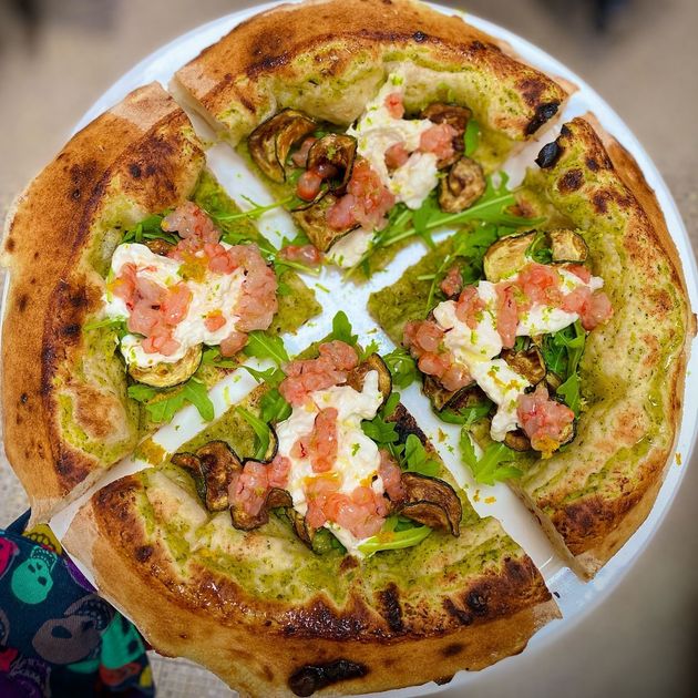 Una pizza con tanti condimenti è servita su un piatto bianco.