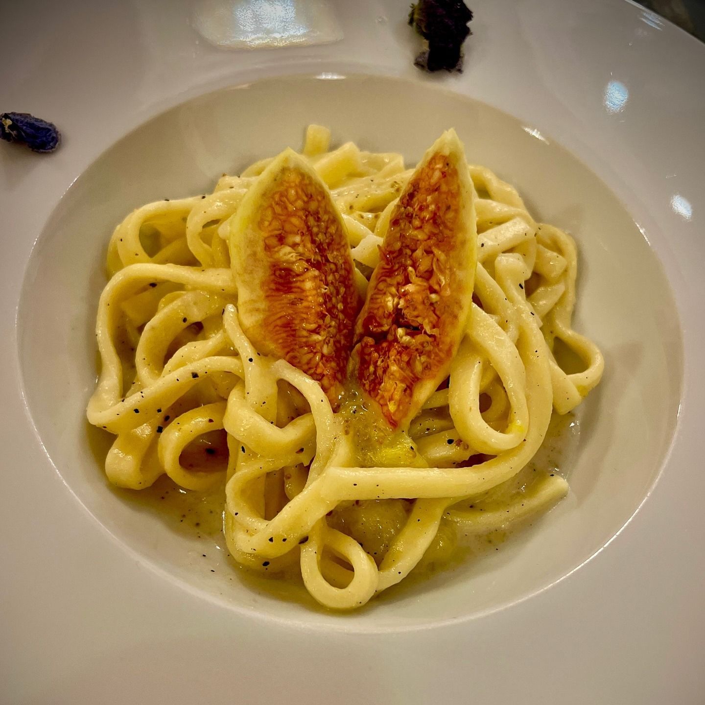 Un piatto bianco con sopra delle tagliatelle e un pezzo di frutta.