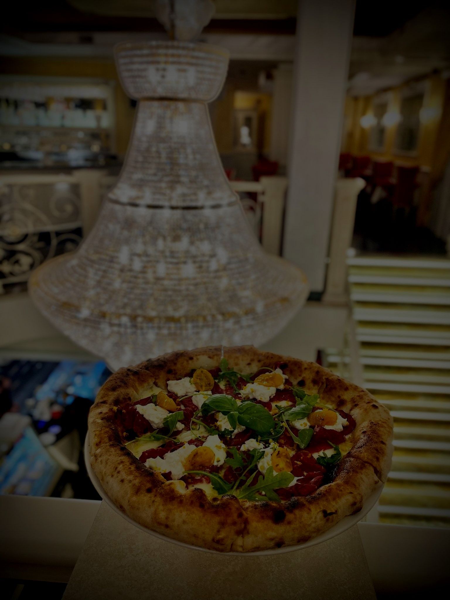 Una pizza è appoggiata su un piatto davanti a un lampadario.