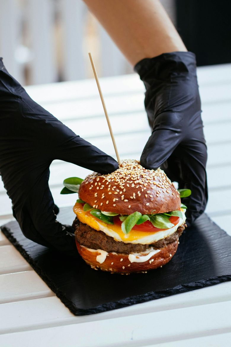Una persona che indossa guanti neri tiene un hamburger infilzato su uno stuzzicadenti.
