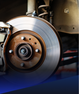 A close-up of a rusty car brake rotor and brake caliper assembly in a garage setting.  | Heaven Sent Automotive