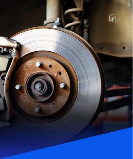 A close-up of a rusty car brake rotor and brake caliper assembly in a garage setting.  | Heaven Sent Automotive