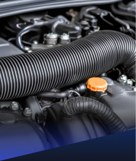 Close-up of a car engine bay featuring black ribbed air intake hoses and an orange oil filler cap. | Heaven Sent Automotive
