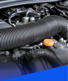 Close-up of a car engine bay featuring black ribbed air intake hoses and an orange oil filler cap. | Heaven Sent Automotive