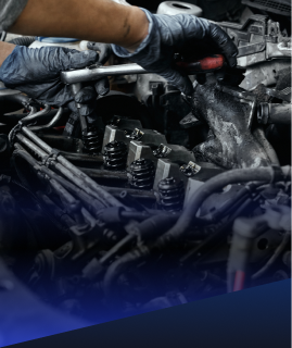 A close-up of a mechanic’s hands in black gloves using a wrench to perform maintenance on an open car engine. | Heaven Sent Automotive