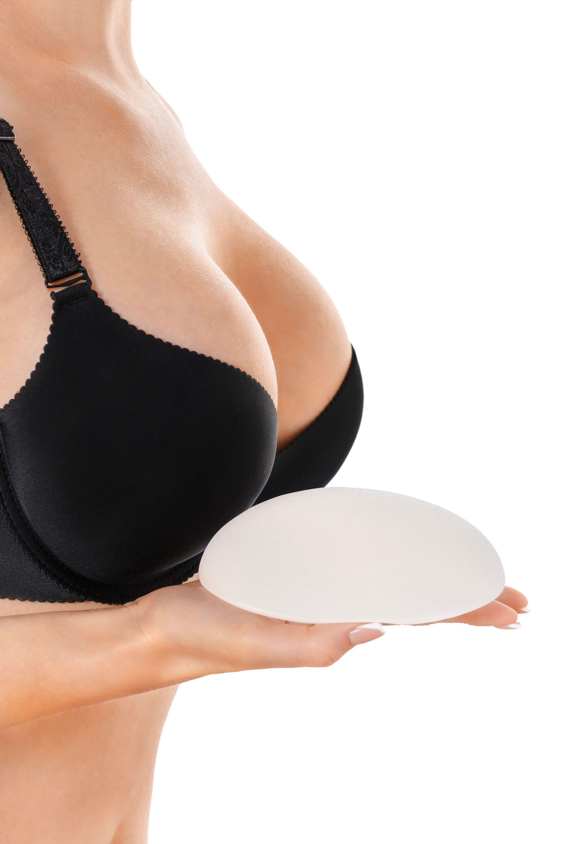 A person wearing a black bra holding a breast implant in their palm.