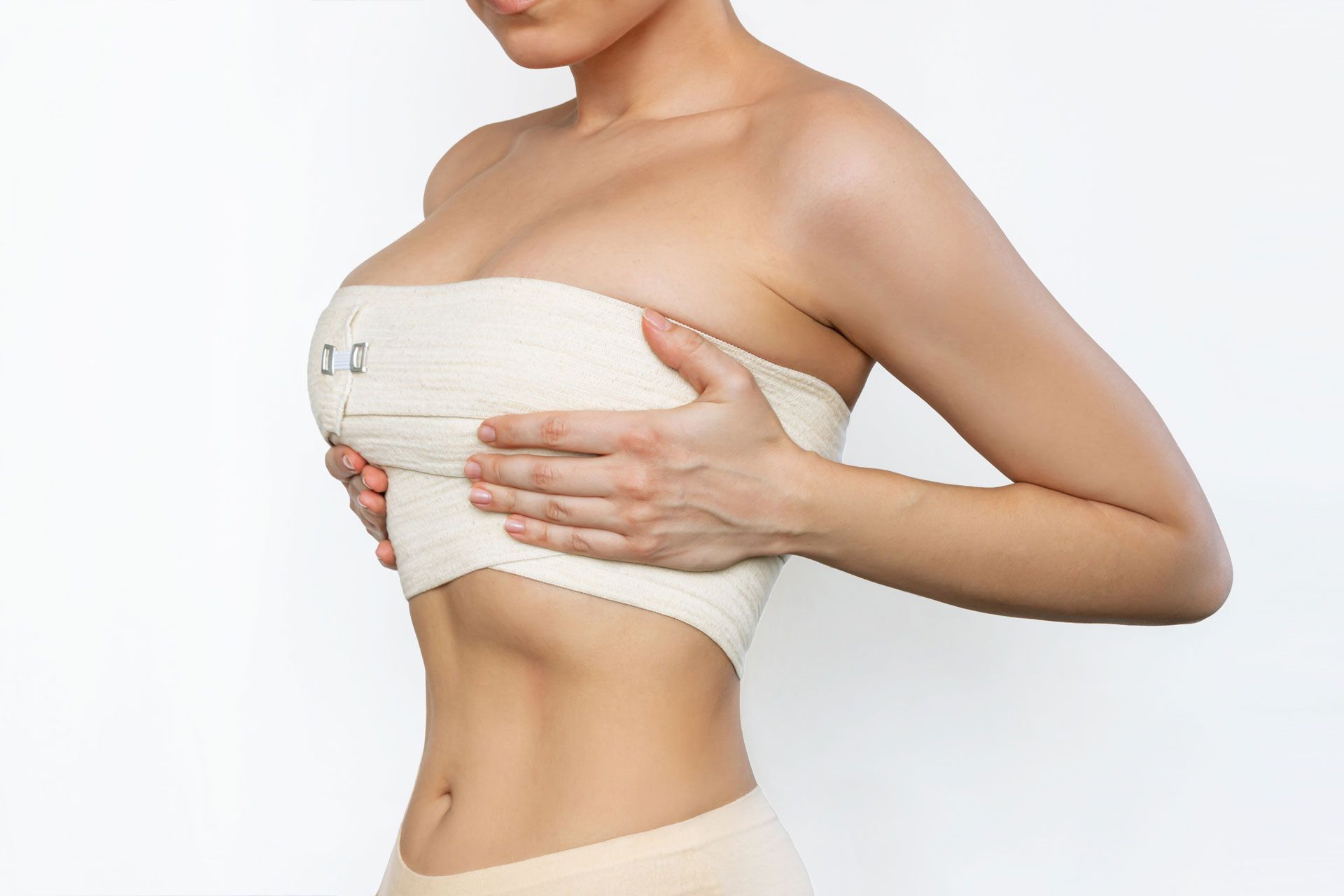 A person in a neutral-colored compression garment for the chest, holding their chest with both hands.