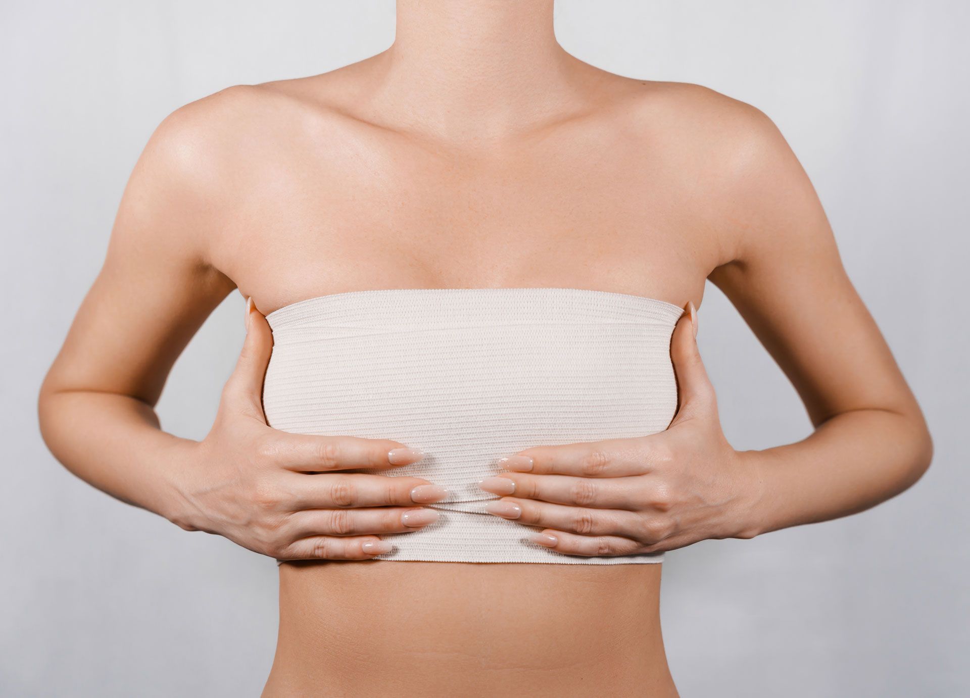 A person with a neutral expression holding their chest, which is wrapped in a beige elastic bandage.