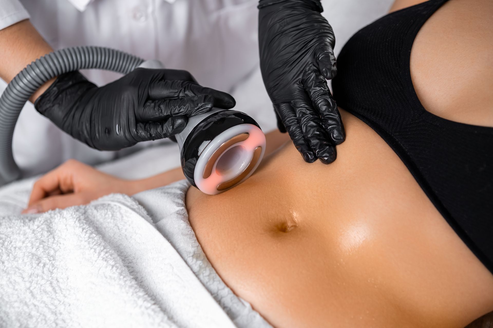 Gloved hands using a glowing handheld device on a person’s bare abdomen during a skin treatment