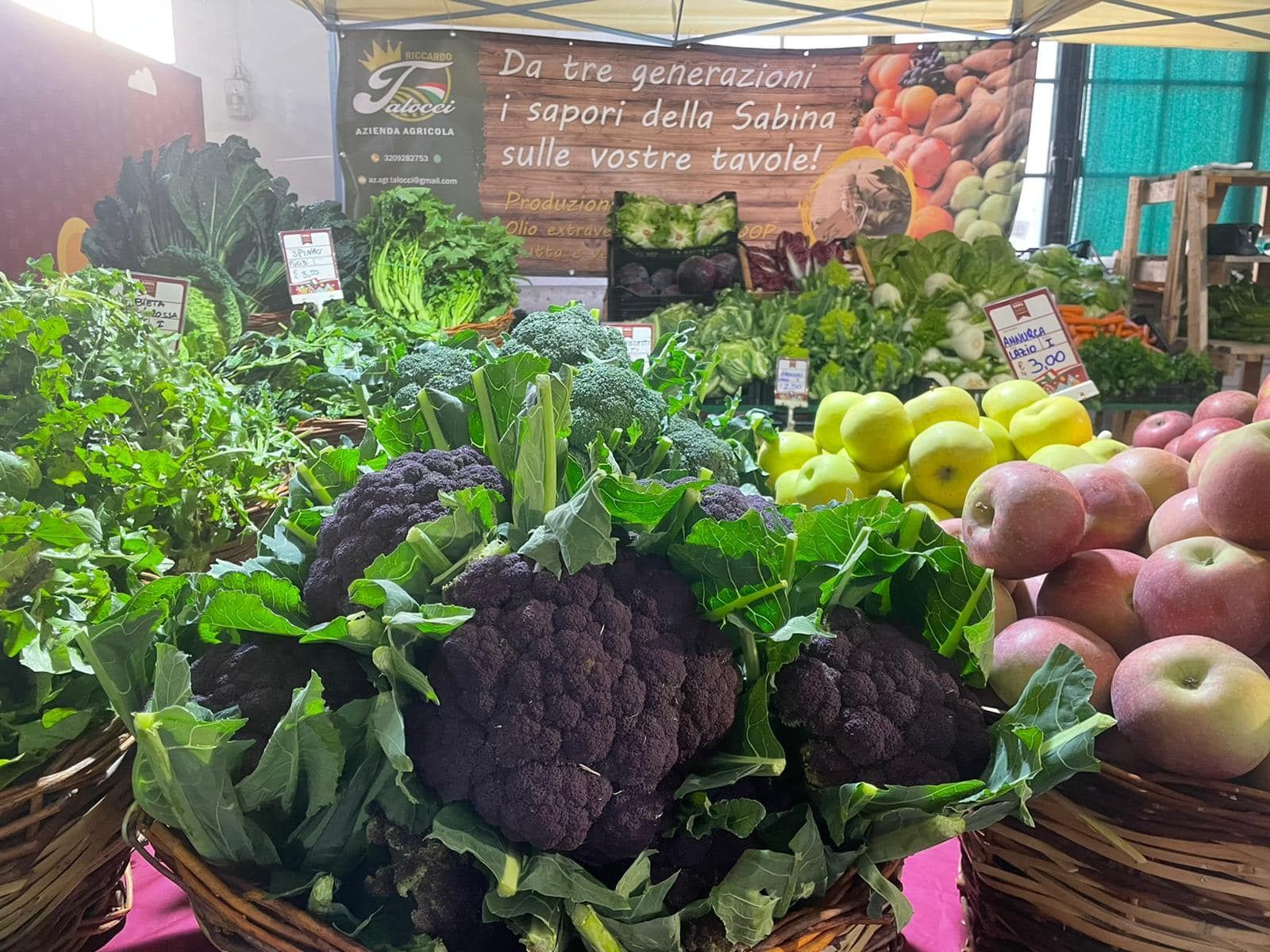 Prodotti freschi su una bancarella del mercato: cavolfiori, cavoli, mele e verdure.