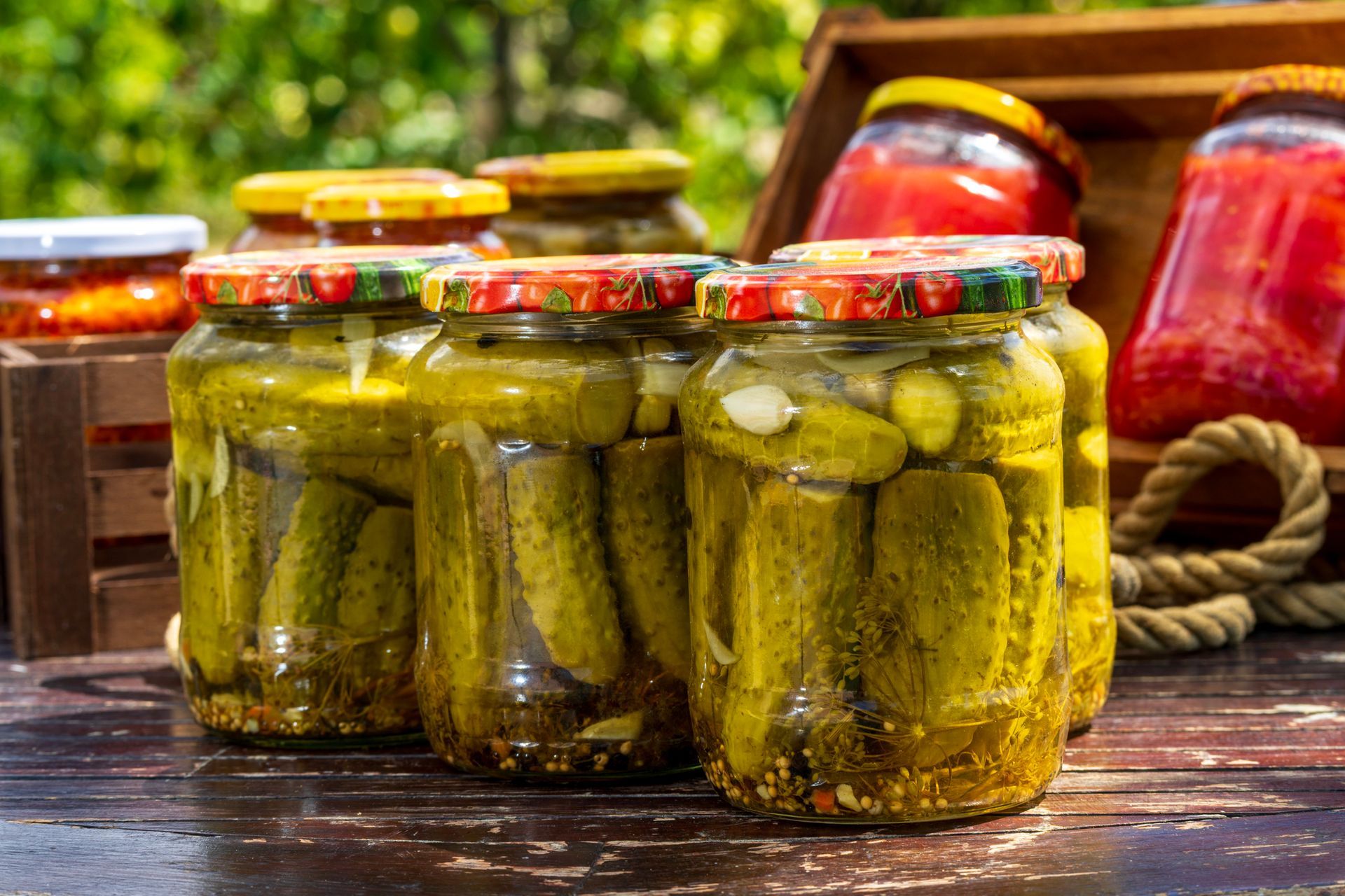 Barattoli di sottaceti fatti in casa e conserve di pomodoro su una superficie di legno, all'aperto.