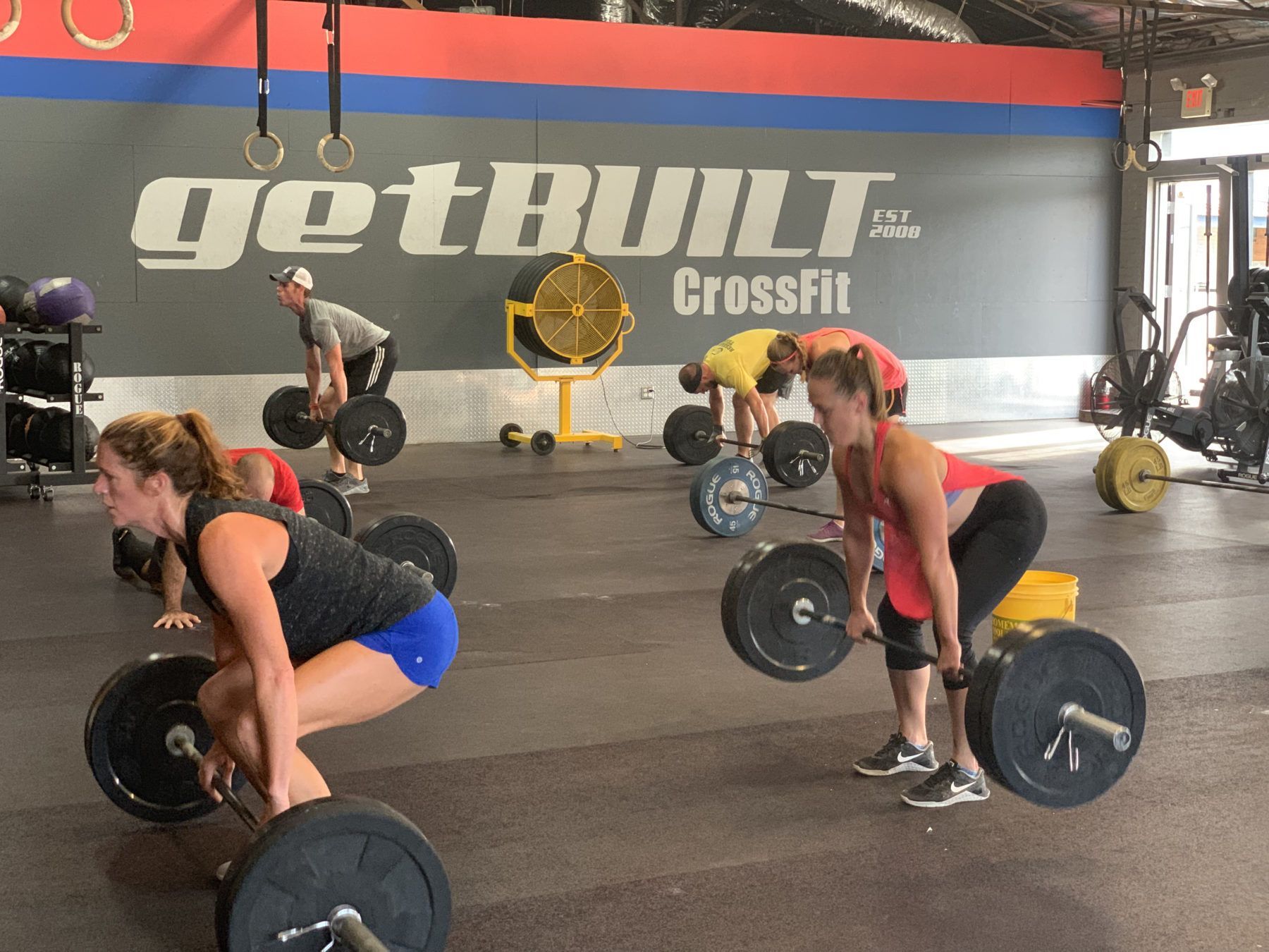 A group of people are lifting weights in a gym called getbuilt crossfit