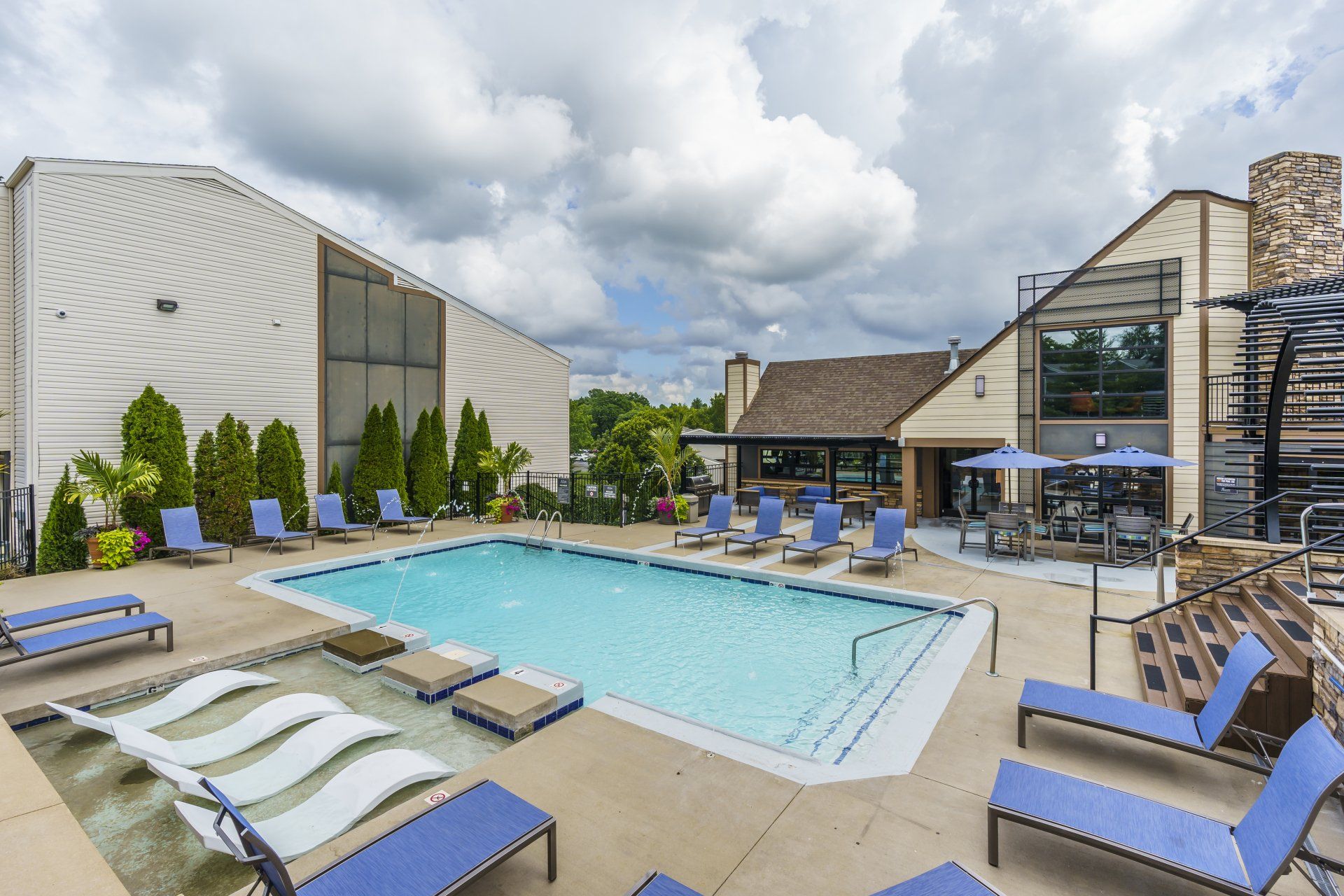 A large swimming pool surrounded by lounge chairs and umbrellas in front of a building.