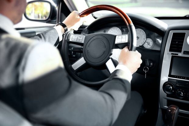 A man in a suit is driving a car with a wooden steering wheel.