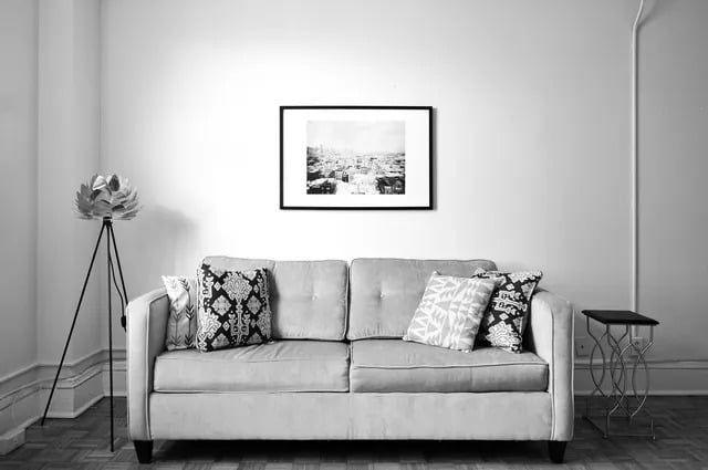 Gray sofa with patterned pillows, artwork, and lamp against a white wall.