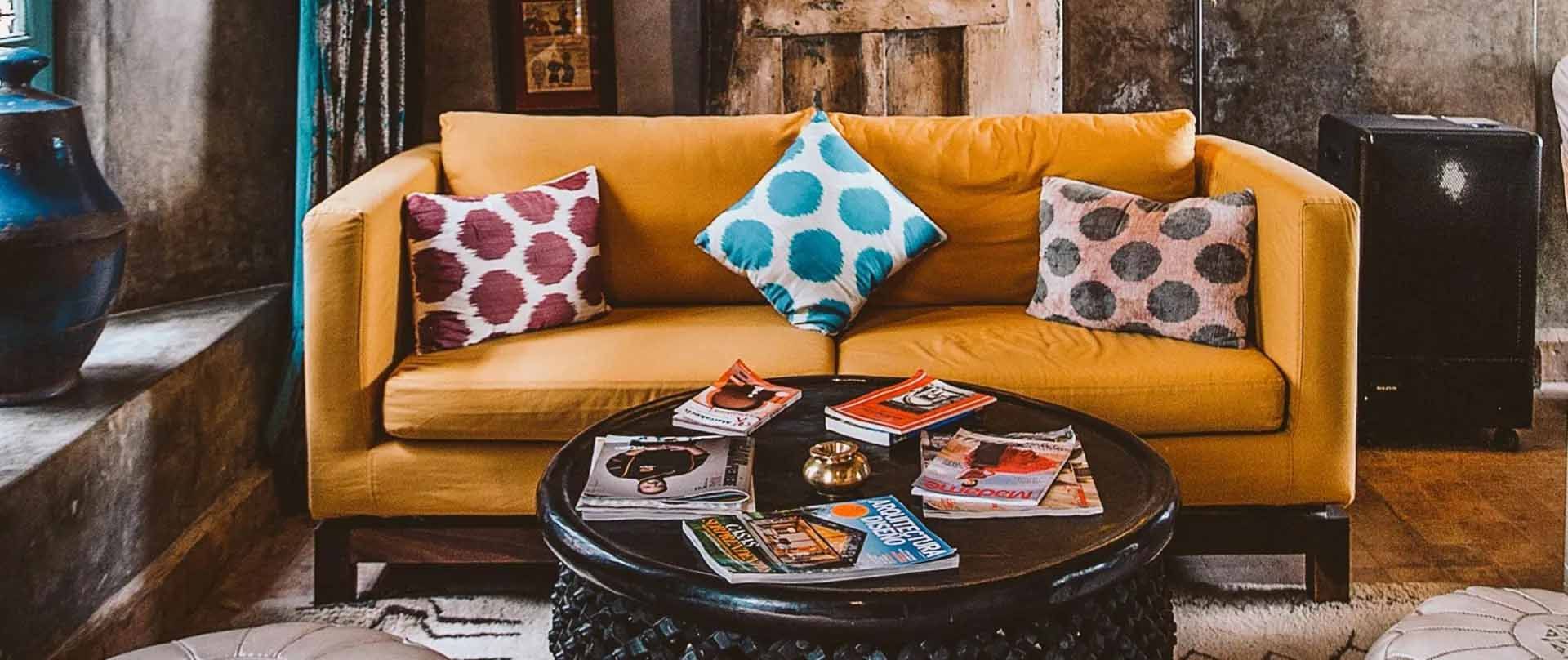 Yellow sofa with patterned pillows, round coffee table with books and a decorative tray.