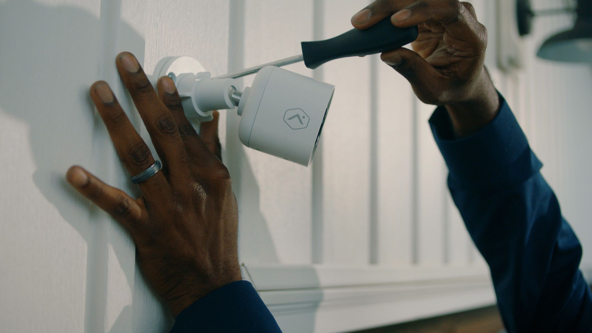 A man is installing a security camera on a wall with a screwdriver.