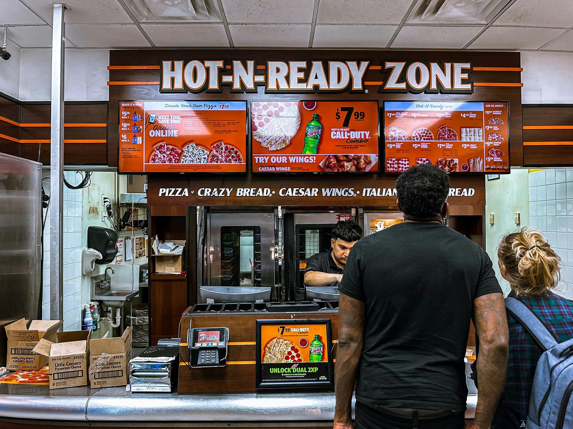 A man and woman are standing in front of a hot n ready zone restaurant