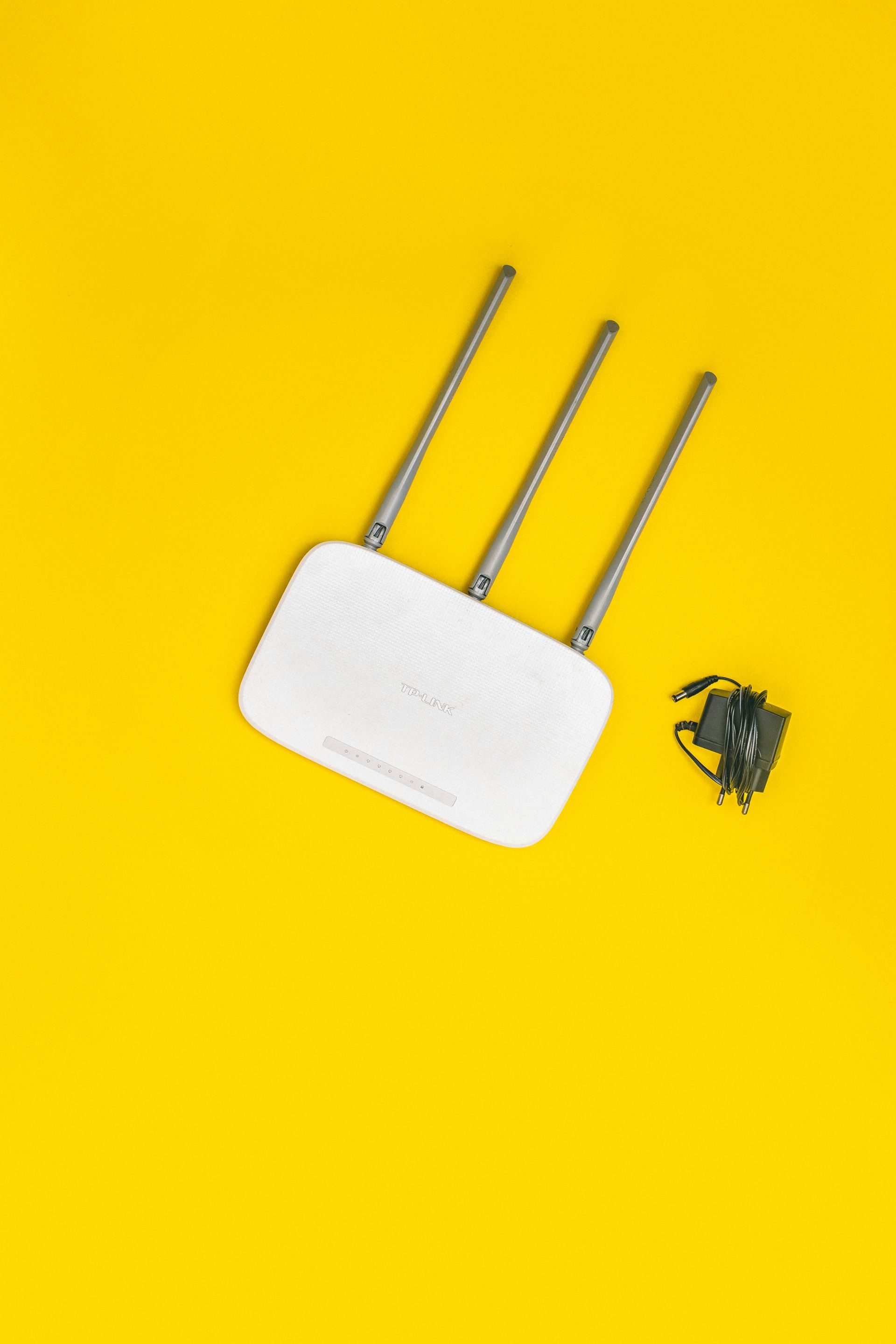 A white router with three antennas and a charger on a yellow background.