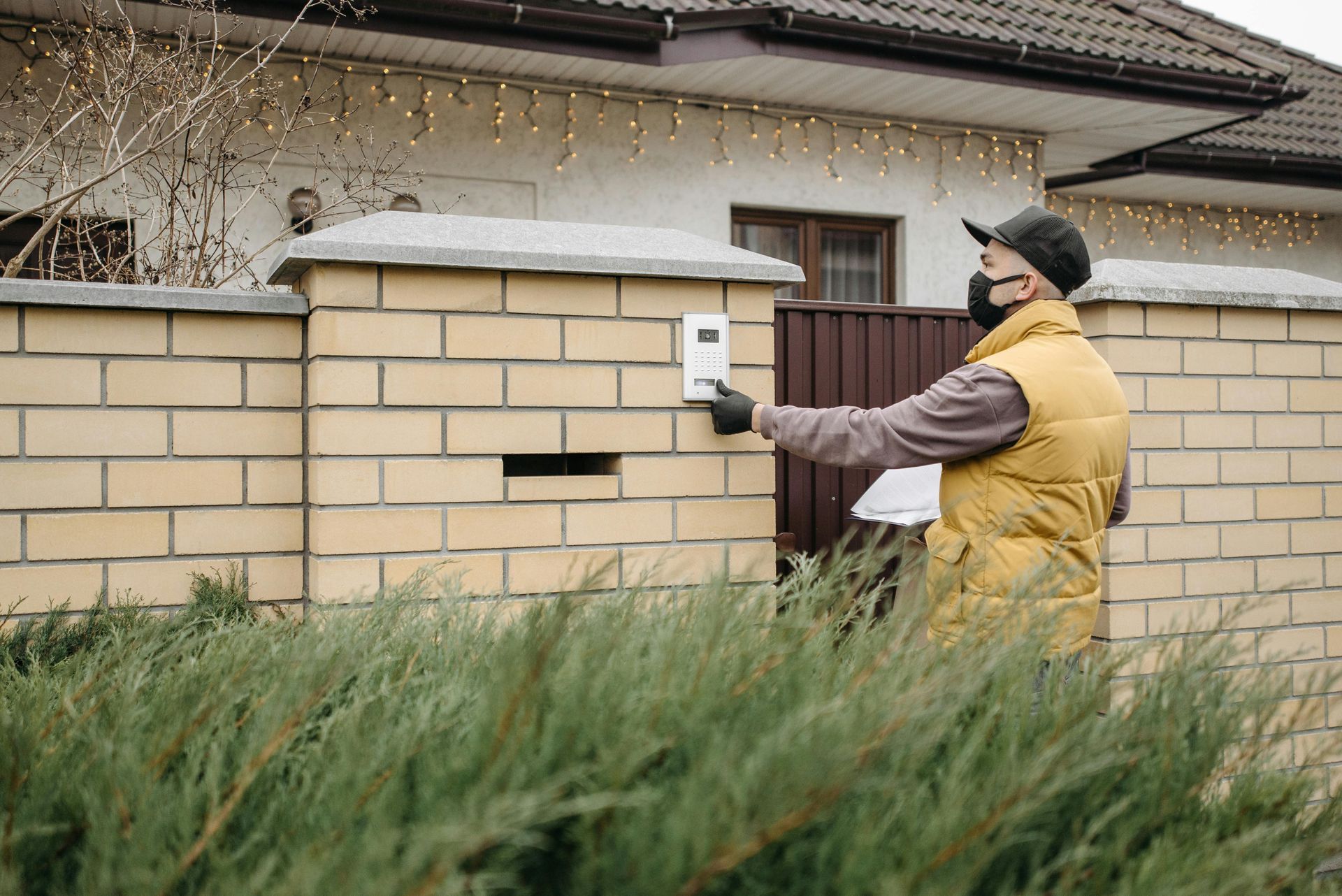 A man wearing a mask is ringing a doorbell outside of a house.