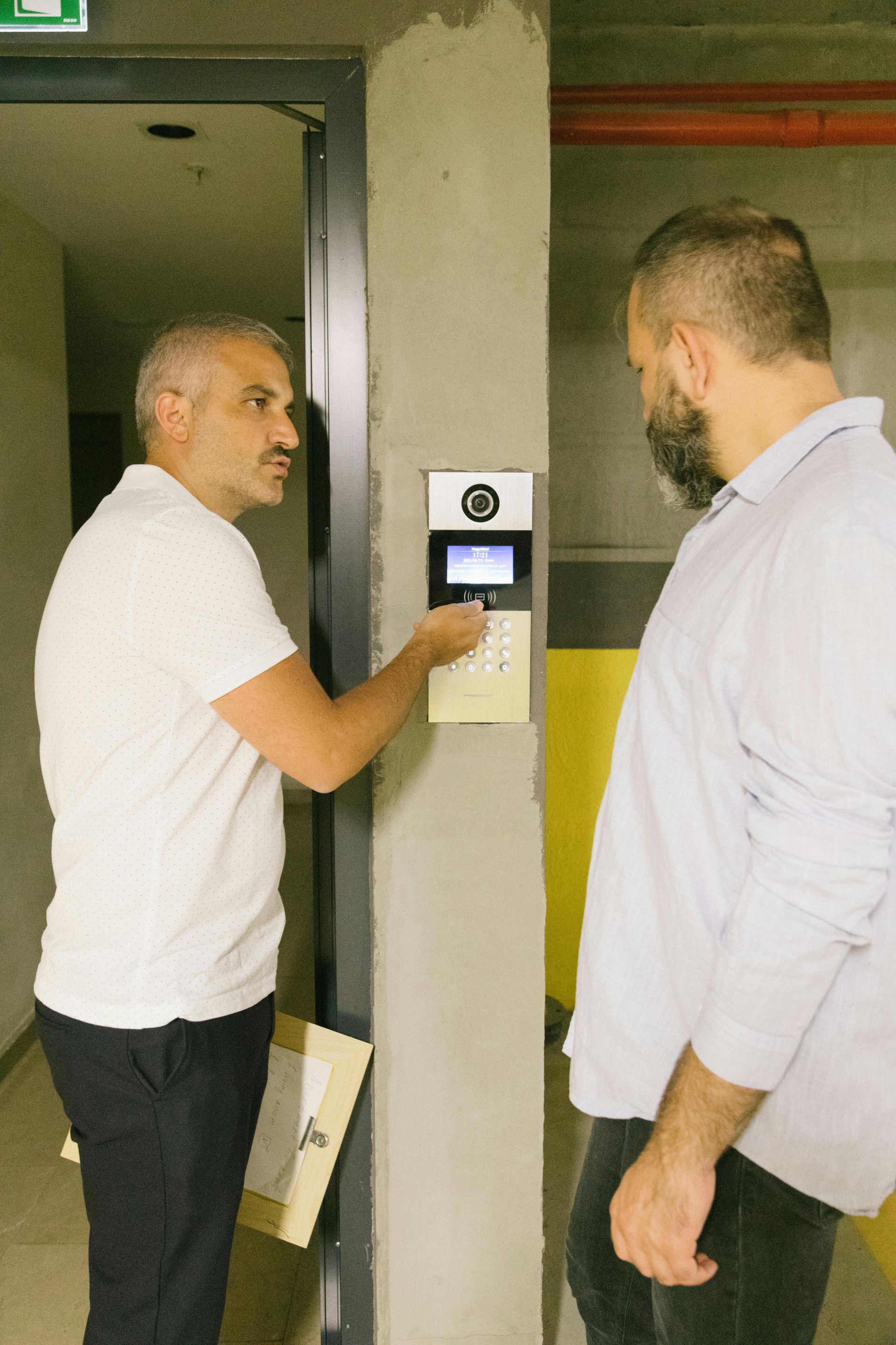 Two men are standing next to each other and one of them is pressing a button on a wall.