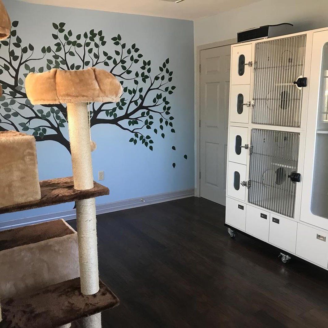A room with a cat tree and a painting of a tree on the wall.