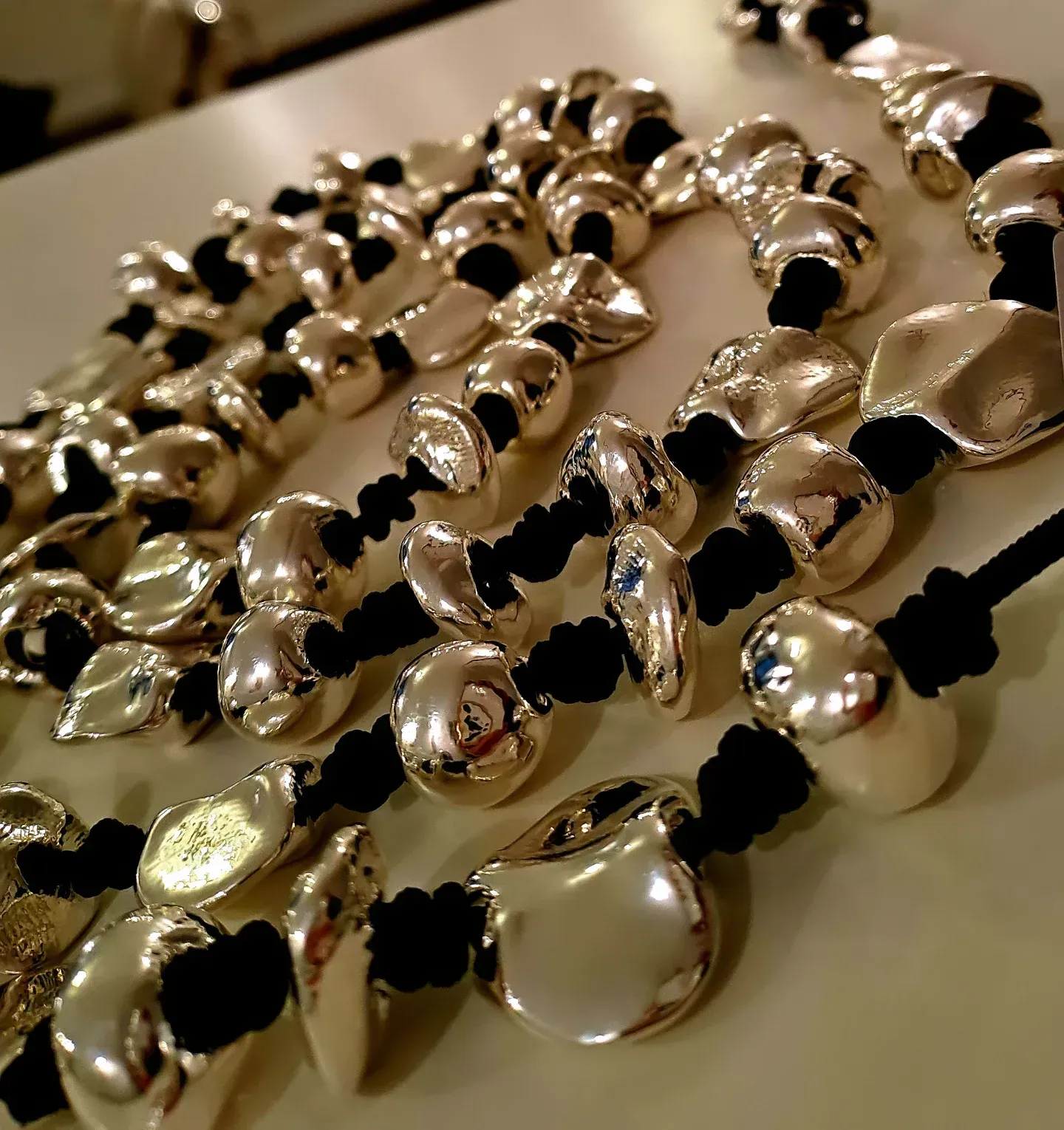 Primo piano di diverse collane con perline irregolari color argento su cordini neri.