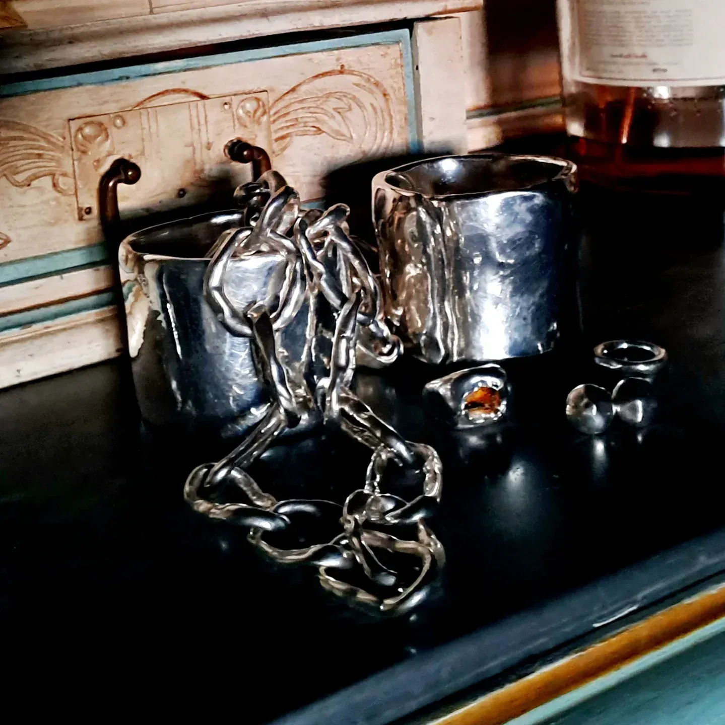 Gioielli in argento su una superficie scura, tra cui due braccialetti, una catena e due anelli.